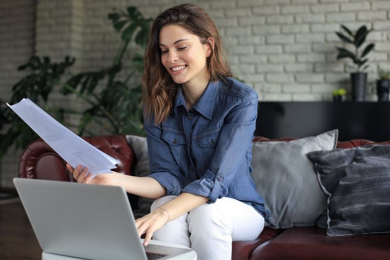 Donna che lavora a un computer con un documento stampato in mano