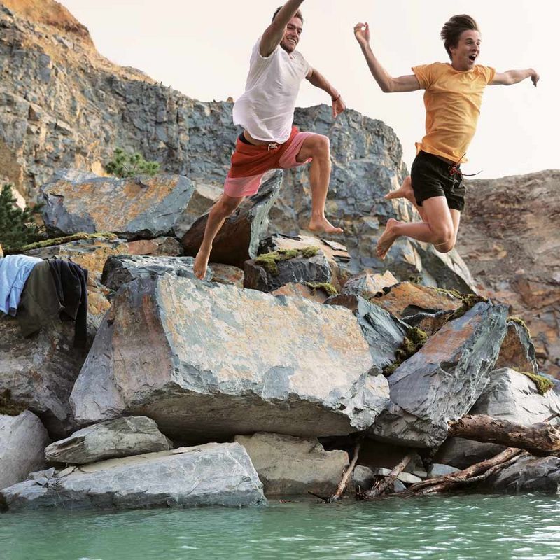 Two friends jumping off rocks into cold lake