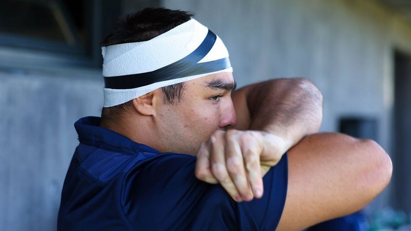 A rugby player in profile with a bandaged head looks to the right 