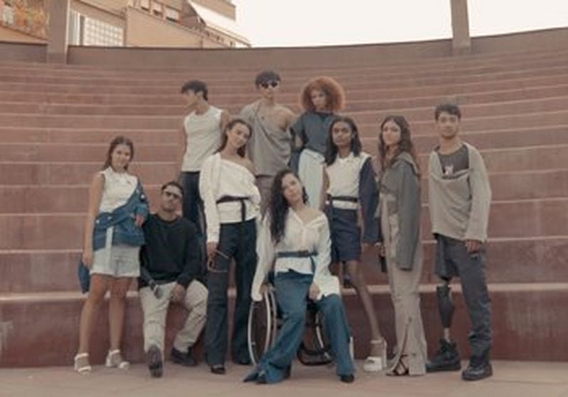 Ten models pose in front of an amphitheatre-style set of steps. They are all wearing clothes from the Adaptive collection – jeans, shorts, belted shorts and utilitarian trousers and jackets. In the centre, one model sits in a wheelchair.
