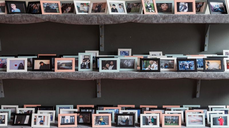 Dozens of framed photographs on three shelves, one above the other.