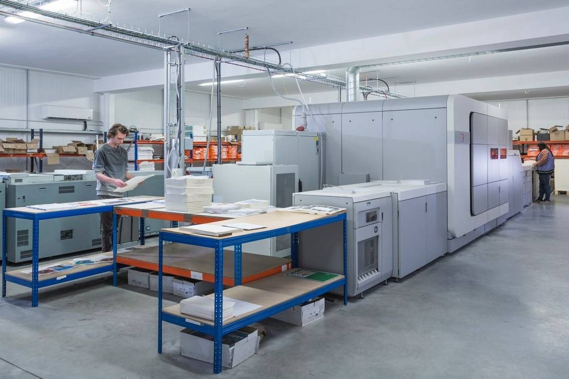 People in background work at industrial book printing equipment in warehouse