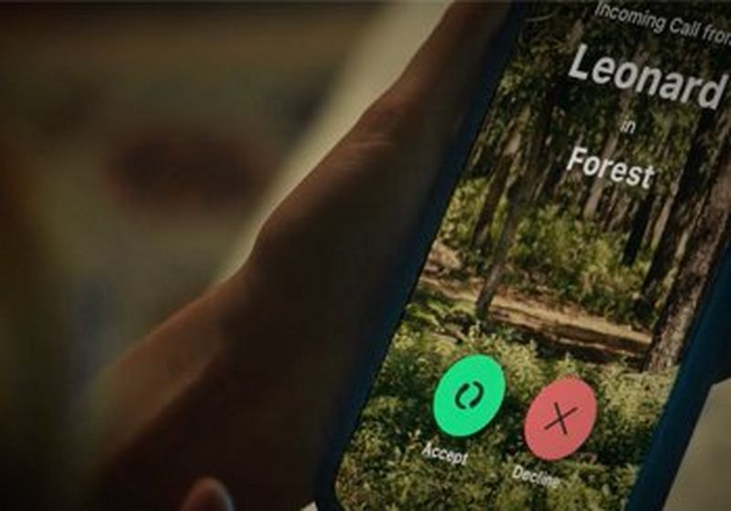 A hand holds a phone. On it shows an incoming call from “Leonard in Forest”, a green button to accept, a red button to decline. The background photograph is an opening on a forest of green trees and foliage.
