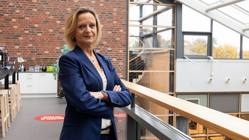 Camilla Overödder stands in an office with her arms crossed. She has mid length blonde hair and wears a navy-blue suit jacket and pale top.