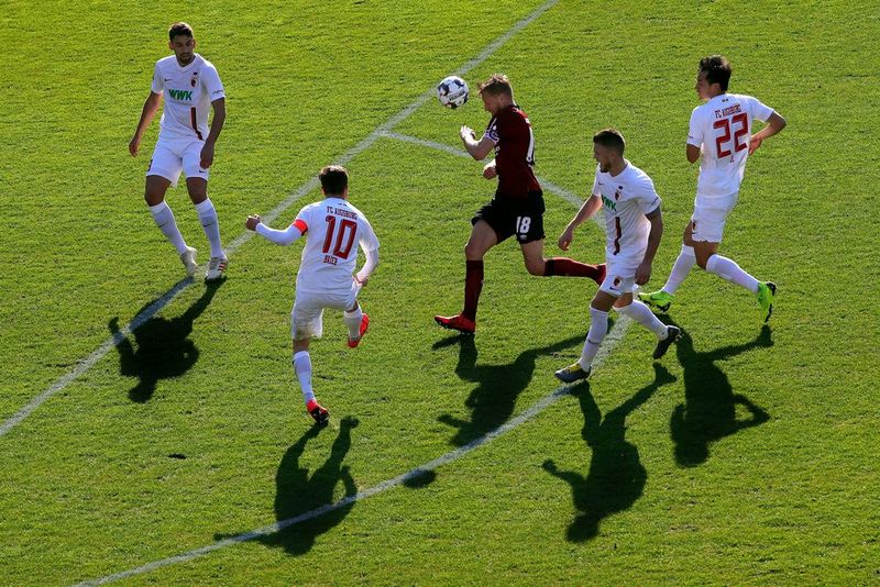 Four football players in white surround one player in red and black in a closely cropped shot.