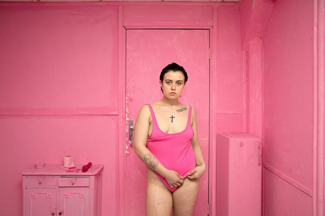 A tattooed woman named Agata stands in a pink bodysuit in a room which is also entirely pink. Taken by Canon Ambassador Bieke Depoorter on a Canon EOS 5D Mark IV.