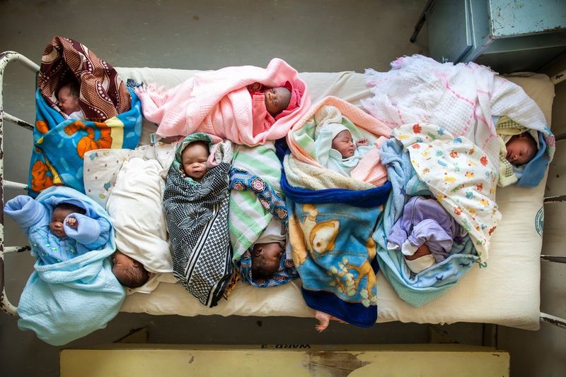 Multiple babies lie swaddled in patterned fabrics, on a small old bed. Taken by Lieve Blancquaert on a Canon EOS 5D Mark II.