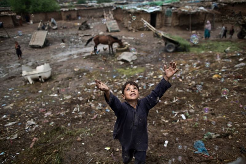 A young Afghan refugee boy jumps to catch a bubble in a poor part of Islamabad, photographed by Muhammed Muheisen on a Canon EOS 5D Mark III.