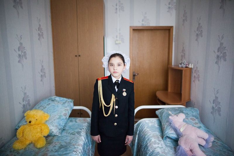 A Russian girl in her cadet school uniform stands in her bedroom, photographed by Pavel Volkov on a Canon EOS 5D Mark II.