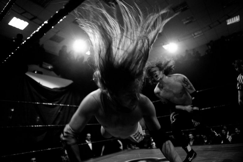 A long-haired wrestler is thrown to the floor by his opponent during a show at the Moscow Wrestling Club, photographed by Pavel Volkov on a Canon EOS 5D Mark II.