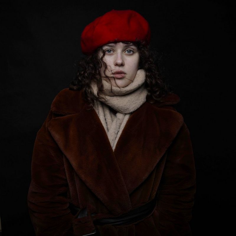 A woman stands against a black background wearing a winter coat and scarf, and a red beret. Taken by Canon Ambassador Piotr Małecki on a Canon EOS 5D Mark IV.