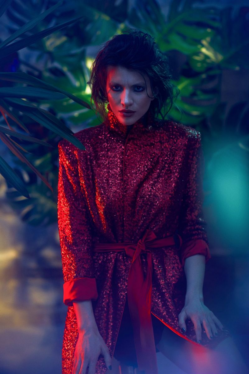 A woman in red stands beneath lush foliage, lit by a red light. Taken on a Canon EOS 5D Mark IV by Canon Ambassador Quentin Caffier.