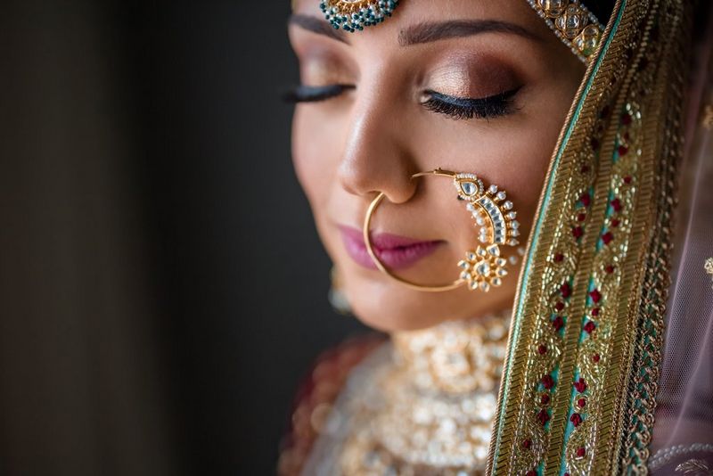 An Indian woman in silk wedding clothes and opulent gold jewellery turns towards the camera with her eyes closed. Taken by Canon Ambassador Sanjay Jogia on a Canon EOS R.