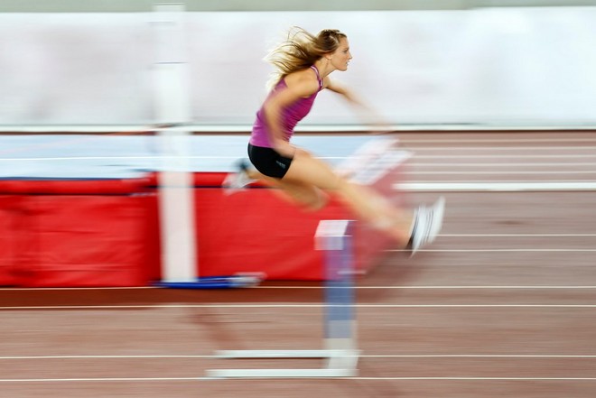 Uma mulher a meio de um salto numa corrida de obstáculos em pista fotografada com efeito de "panning".