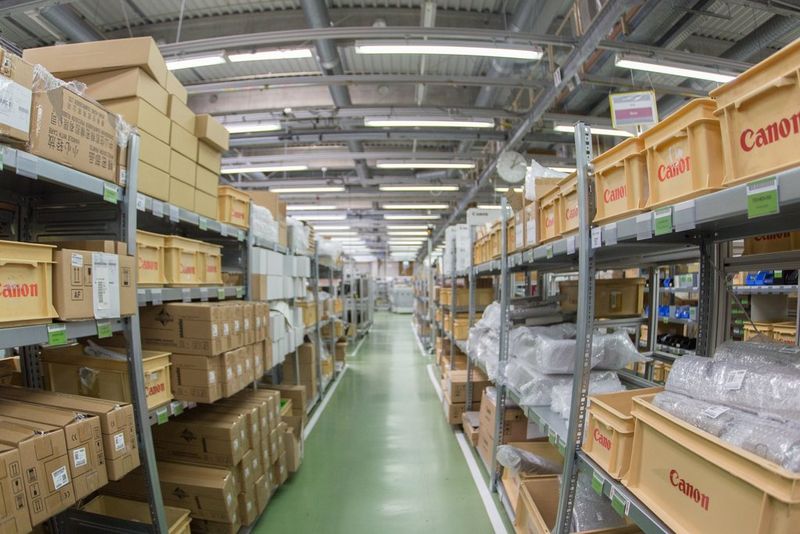  A photo looking down an aisle between rows of shelves in a warehouse, with vertical and horizontal image elements distorted by barrel distortion.