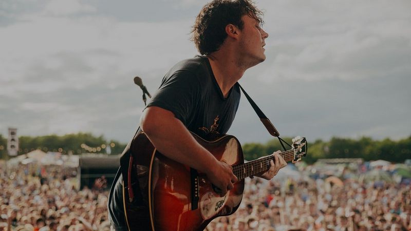 A rock musician on stage at a festival plays the guitar. Photo by Ben Morse.