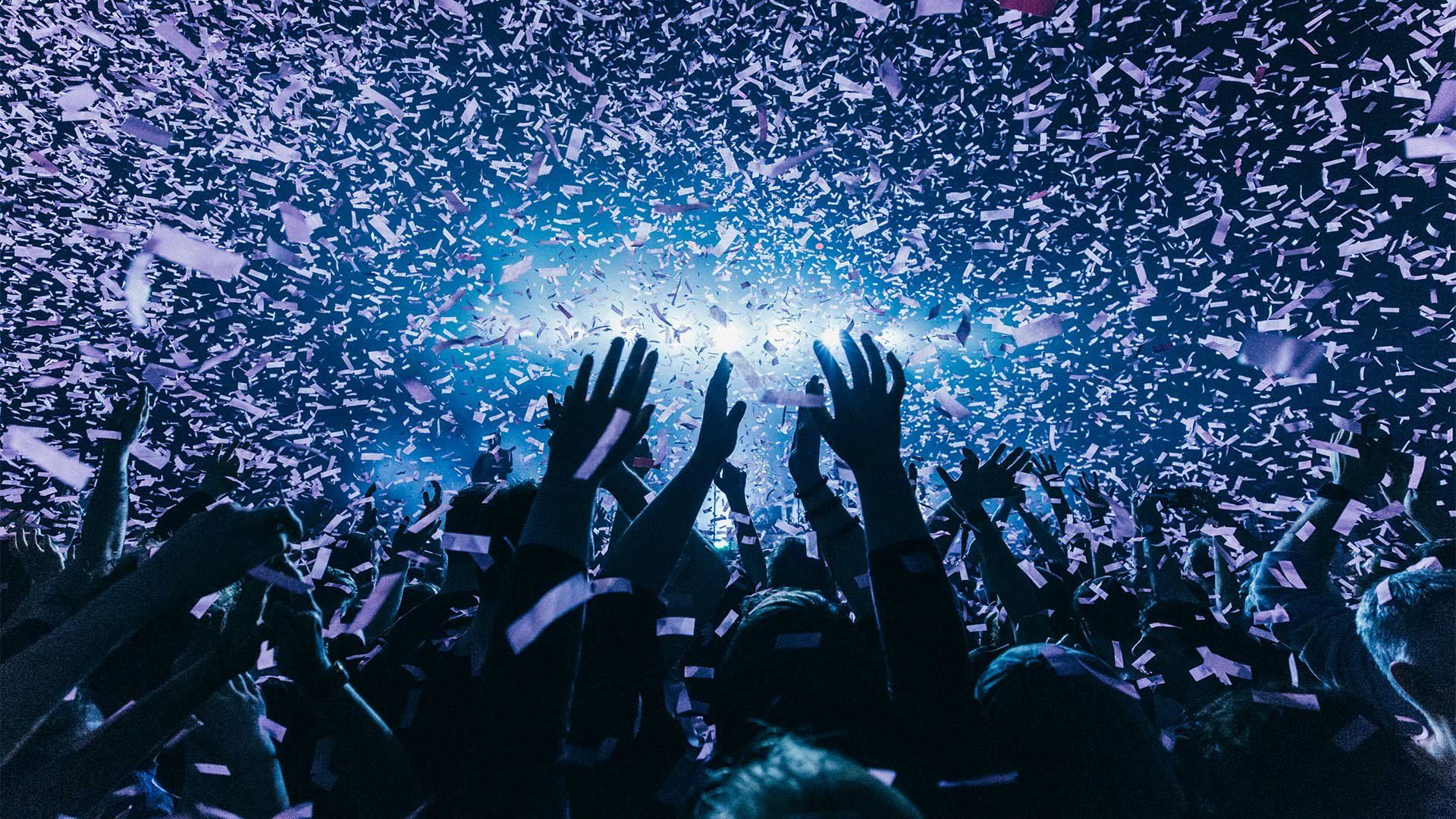 People in a festival audience hold up their hands as confetti showers down on them. Photo by Ben Morse.