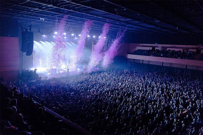 Overhead shot of gig showing confetti exploding out from the stage and towards the audience. Photo by Ben Morse.