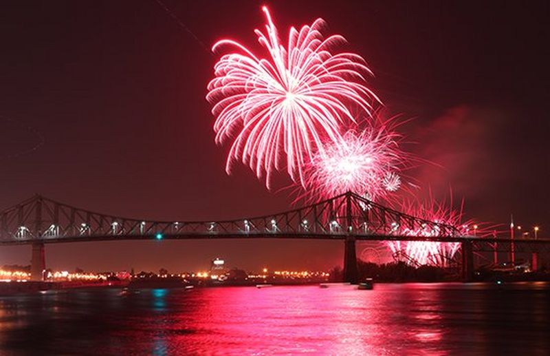 Pink fireworks explode over a bridge, lighting up the water.