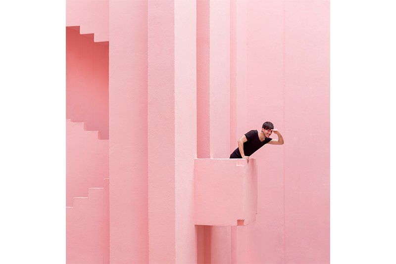 A man in black leans out of a pink balcony in an all-pink building stairwell. Photo by Daniel Rueda and Anna Devís.