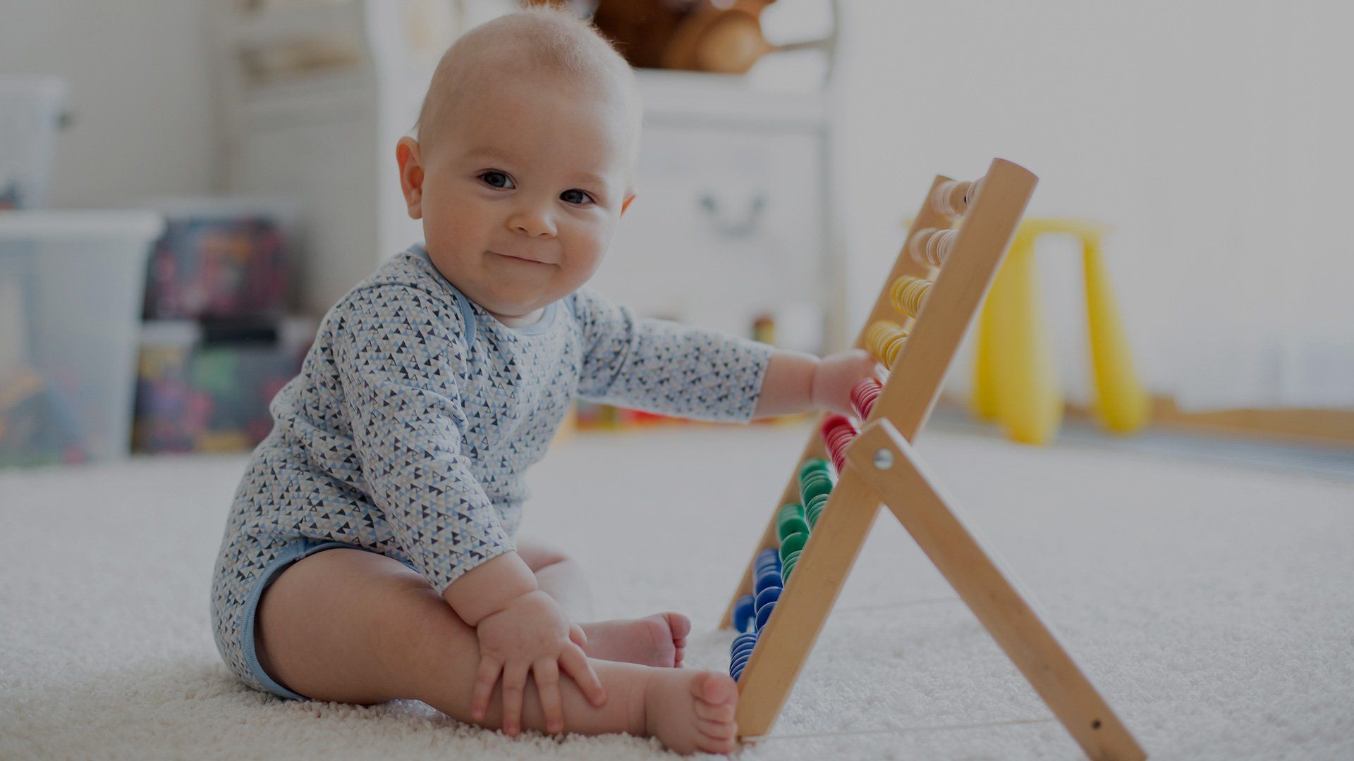 A baby sits upright, playing with coloured beads on an abacus.