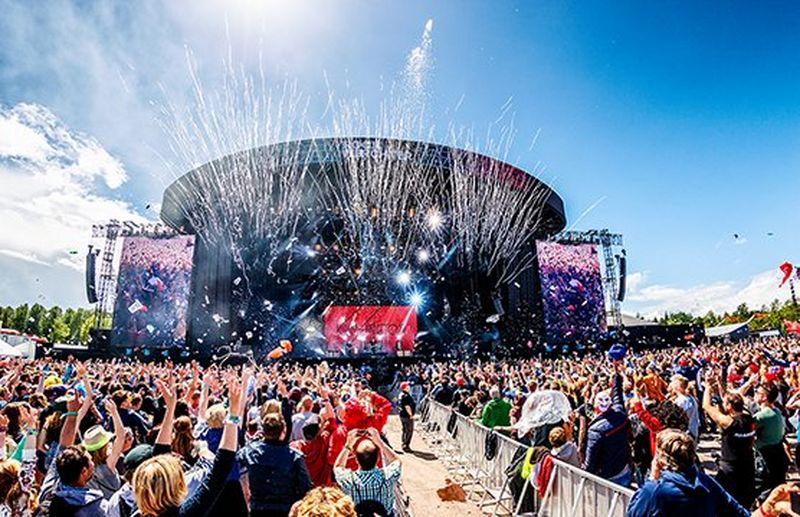 A crowd of people watch music on a huge festival stage in the sun. Photo by Bart Heemskerk.