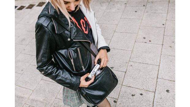 A girl wearing a leather jacket and skirt gets a compact camera out of her handbag.
