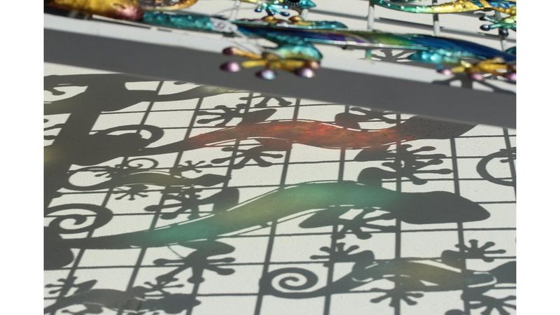 Some lizard-shaped sculptures cast shadows on a grey wall.