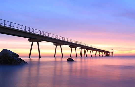 A long jetty, viewed from water level at dusk, stretches into the sea.