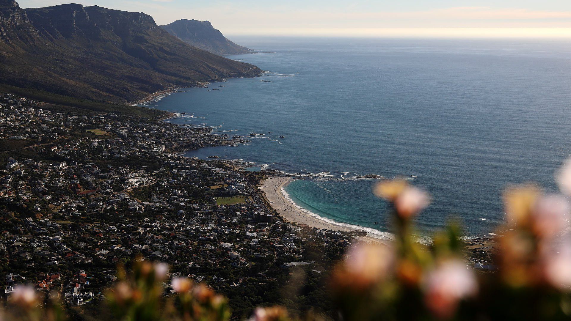 A coastal village in South Africa viewed from a high vantage point, with hills in the distance and the sea stretching to the horizon.