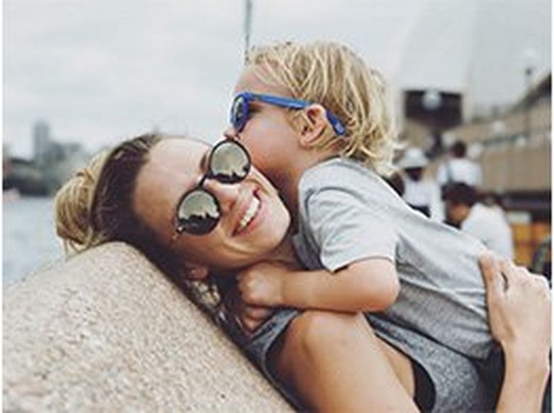 A mother picks her son up to hug, both of them wearing sunglasses. Photo by Christian Anderl.