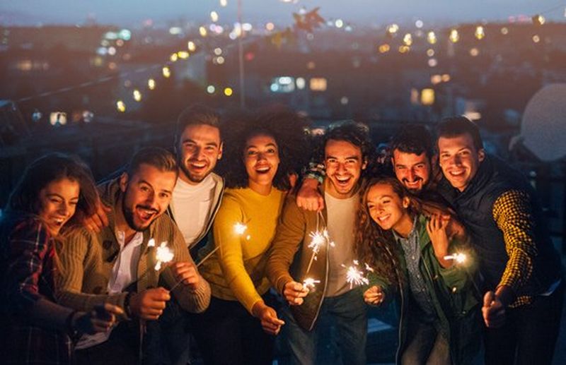 A group of friends pose holding sparklers, facing the camera with their faces illuminated by the sparkler light.