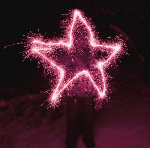 In a long-exposure image, a sillhouetted figure has drawn a bright pink five-pointed star with a sparkler.