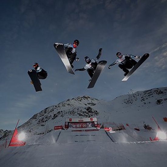 Four people leap through the air on snowboards.