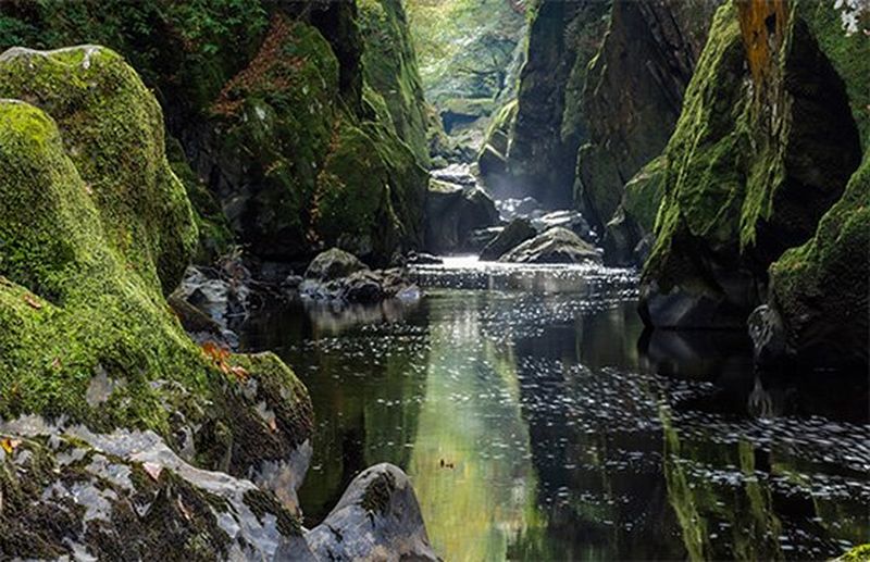 A narrow river or stream flanked by moss-covered rocks.