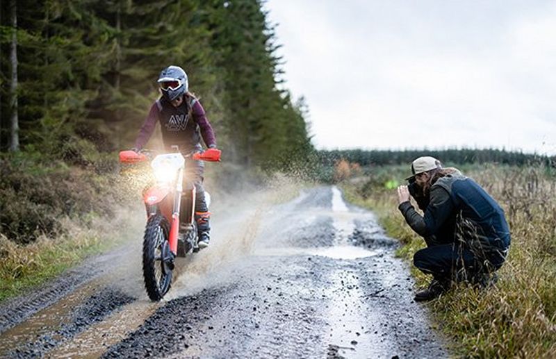 A dirt bike heads towards the camera spraying muddy water in its wake.