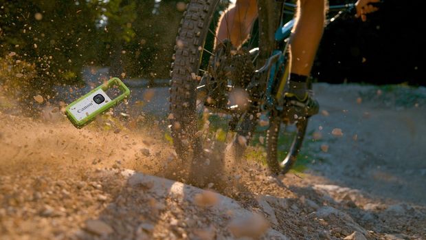 A green Canon IVY REC tumbles into the sand in the wake of a mountain bike.