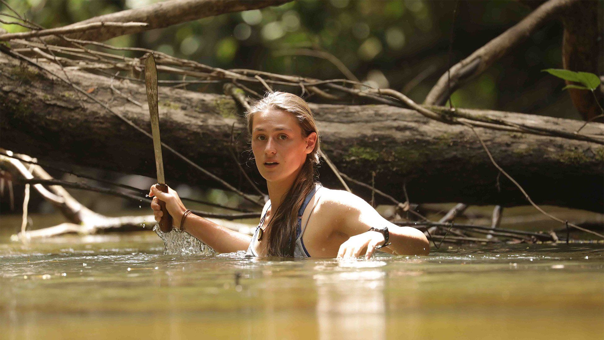 Adventurer Laura Bingham stands chest deep in the Essequibo River, holding a machete aloft. Photograph by Jon Williams.
