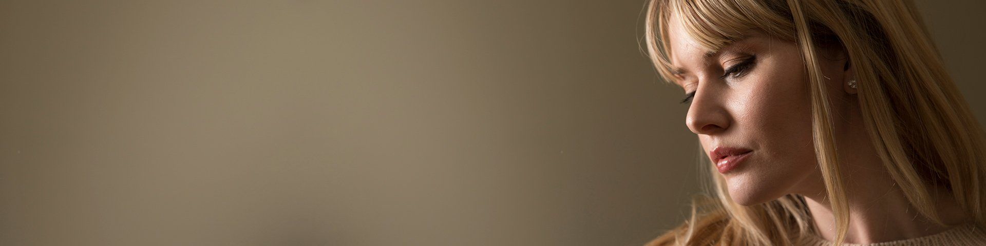 A woman against a grey wall is lit softly.