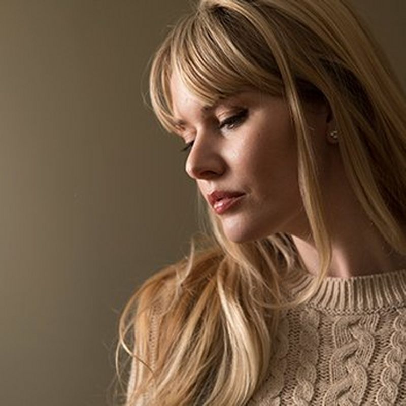 A woman against a grey wall is lit softly.