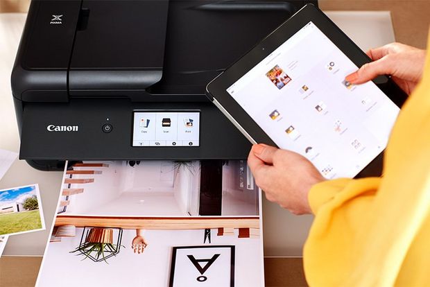 Woman standing next to a printer and operating it via her tablet.