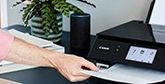 A user takes a printout from a black Canon printer, which has an Amazon Echo smart speaker next to it.