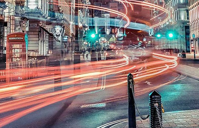 Light trails from car lights race along a city street corner.