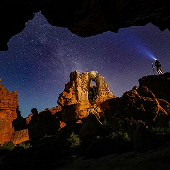 A photographer stands under the night sky in a desert wearing a head torch.