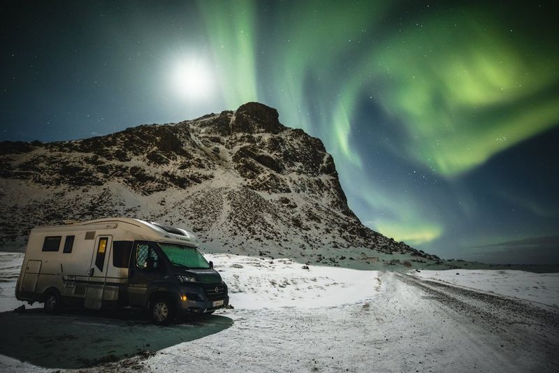The Northern Lights swirl through the night sky above a mountain, with Markus Morawetz's campervan in the foreground.