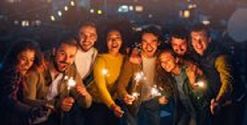 A group of friends pose holding sparklers, facing the camera with their faces illuminated by the sparkler light.