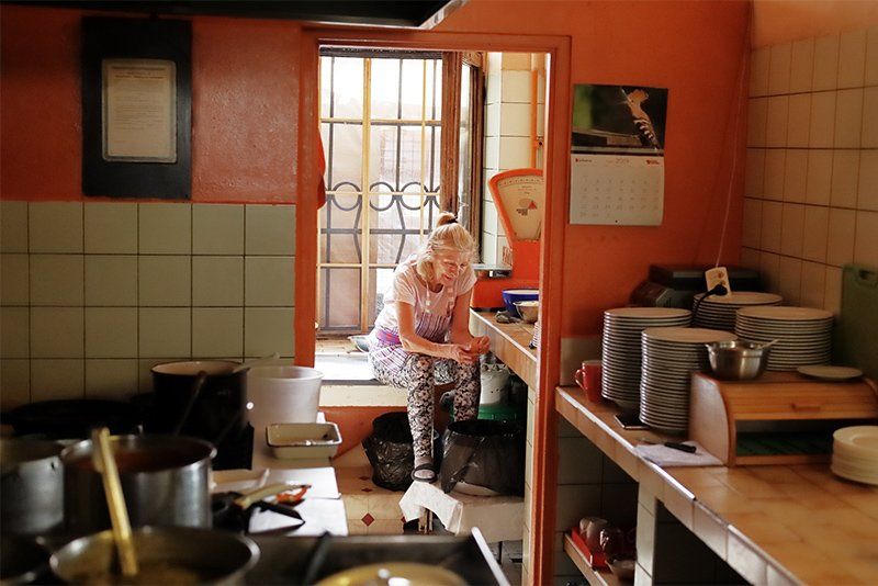 An older woman sits on a windowsill in a commercial kitchen.