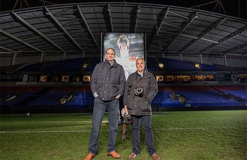 Sports photographer Dave Rogers stands next to rugby player Martin Johnson on the pitch.