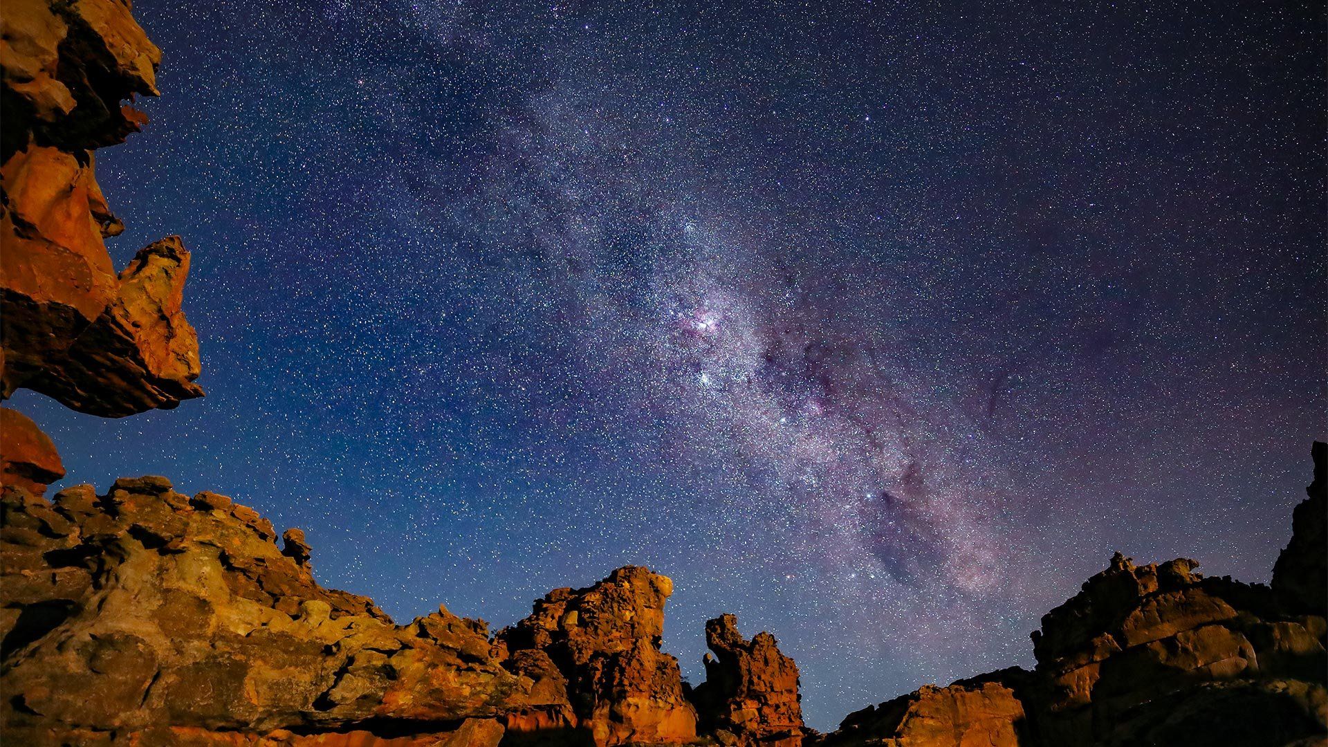 The Milky Way in a star-filled sky, above rugged cliffs in the foreground.
