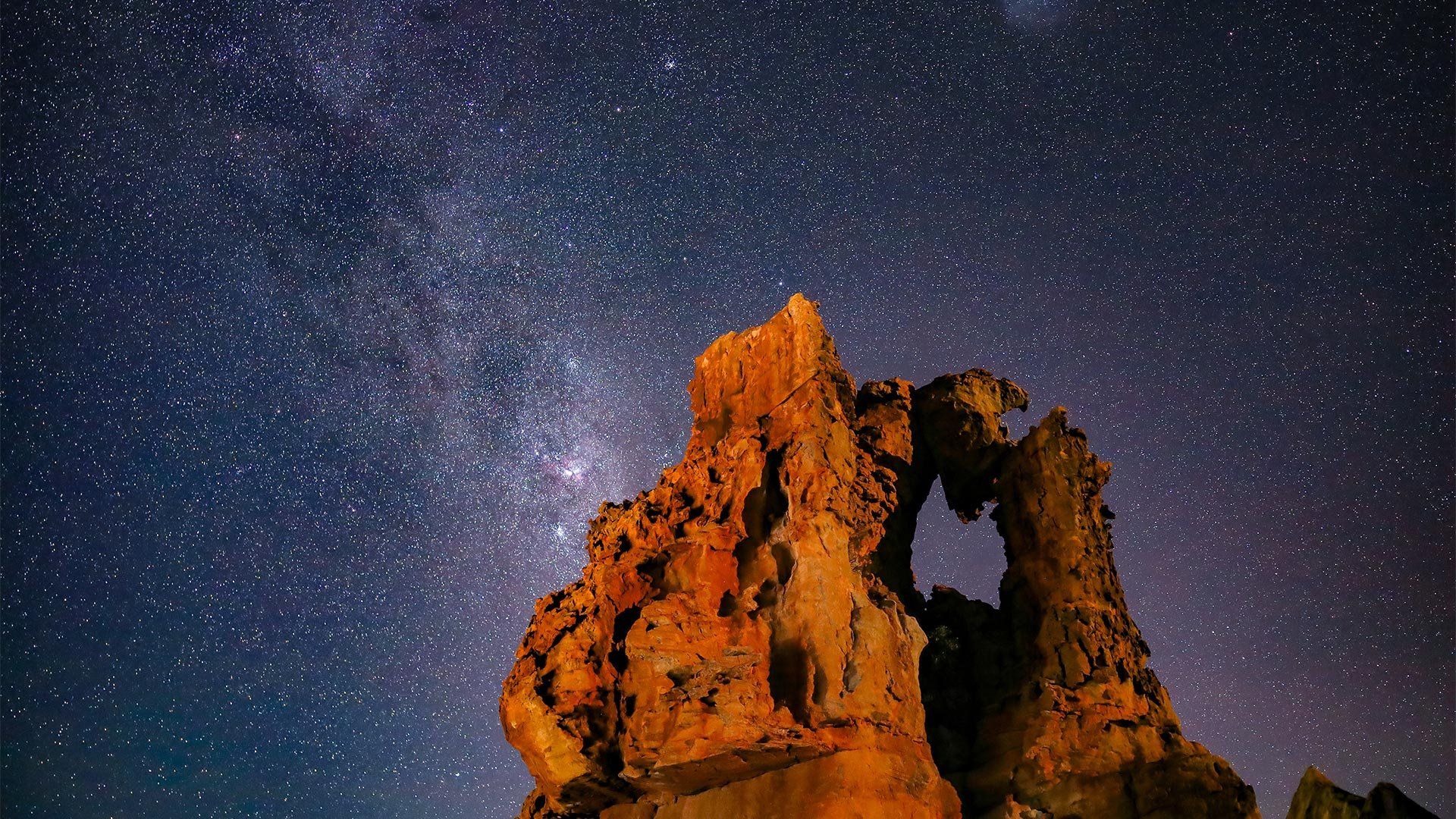 A rock formation standing stark against a sky filled with stars.